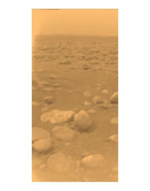 Processed-color Huygens photograph of Titan’s orange surface with rounded pebbles and a hazy horizon