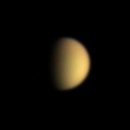 Titan appears as a small orange crescent against black space in a natural-color Cassini image